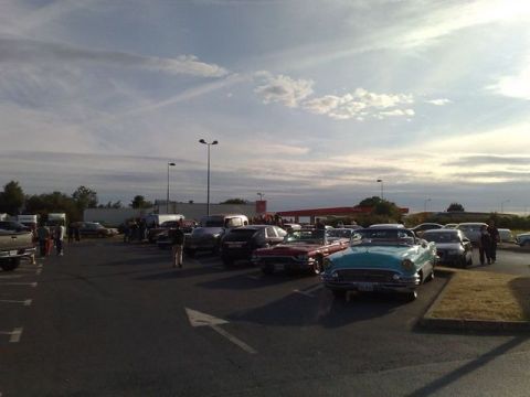 1991 Ford Crown Victoria - A gathering of vehicles, including several classic cars, parked in an outdoor lot under a cloudy sky.