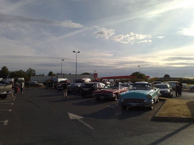 Cars parked in a lot, some are classic models. A blue convertible is in the foreground