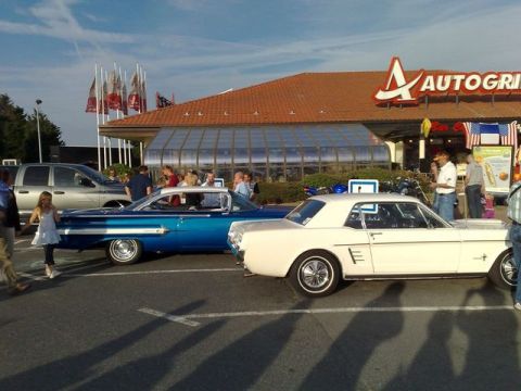 1991 Ford Crown Victoria - A white 1965 Ford Mustang coupe is parked alongside a blue classic car in front of an Autogrill.