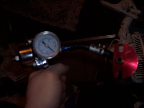 1995 Ford Probe - A fuel pressure regulator with a gauge is held by a hand, with a red fitting visible.
