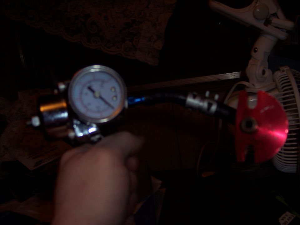 Fuel pressure regulator with gauge and red fitting, held by a hand