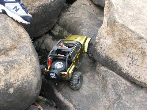 1996 Ford Bronco - A gold Jeep Wrangler is shown navigating a challenging rocky obstacle course, with a spare tire mounted on the rear.