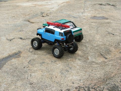 1996 Ford Bronco - Two remote-controlled vehicles, one a blue and white SUV with a kayak on its roof, are parked on a rocky surface.