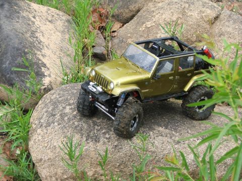 1996 Ford Bronco - A toy Jeep is positioned on a rocky surface with grass and foliage around it.