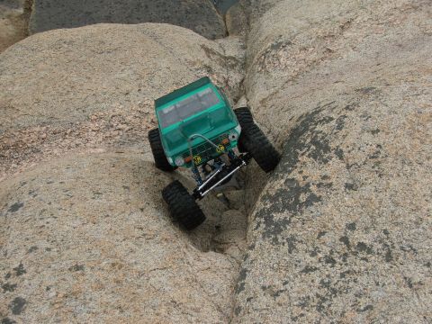 1996 Ford Bronco - A green RC rock crawler is shown navigating a narrow gap between large rocks.
