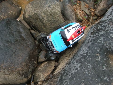 1996 Ford Bronco - A remote control rock crawler with a kayak on its roof navigates a rocky stream bed.