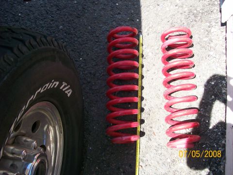 1984 Ford Bronco - Two red coil springs are shown next to a tire, with a measuring tape indicating their size.
