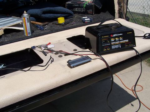 1986 Ford Bronco - A battery charger is connected to wires on an open tailgate, with tools and a spray can nearby.