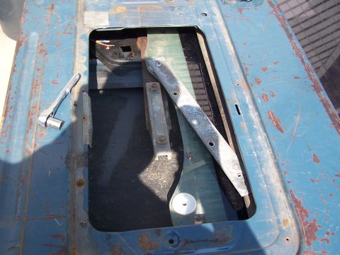 1986 Ford Bronco - Close-up of a tailgate's interior showing the window mechanism and a socket wrench, with visible rust and wear.