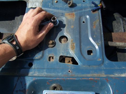 1986 Ford Bronco - Close-up of a hand using a socket wrench on a rusty metal panel, likely part of a vehicle repair.