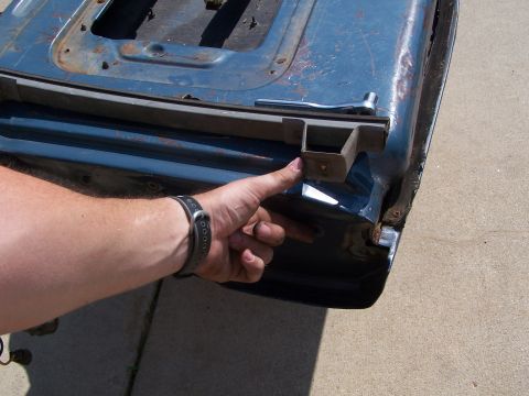 1986 Ford Bronco - Close-up of a blue tailgate's interior, showing a mounting bracket and seal, with a hand indicating a detail.