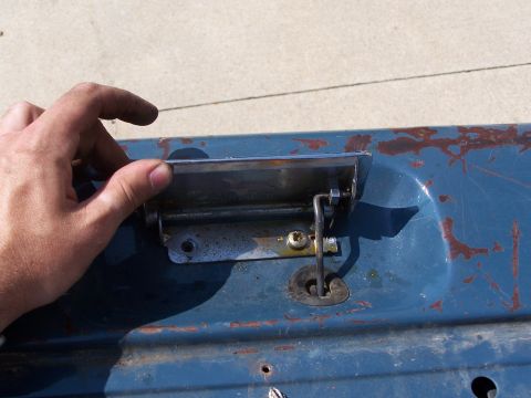 1986 Ford Bronco - Close-up of a blue tailgate handle with visible rust and wear, a chrome pull and keyhole mechanism.