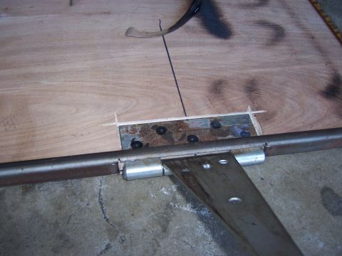 1991 Ford Bronco - A close-up view of a welding table shows a metal hinge attached to a wooden surface, with a metal bar running across the frame.