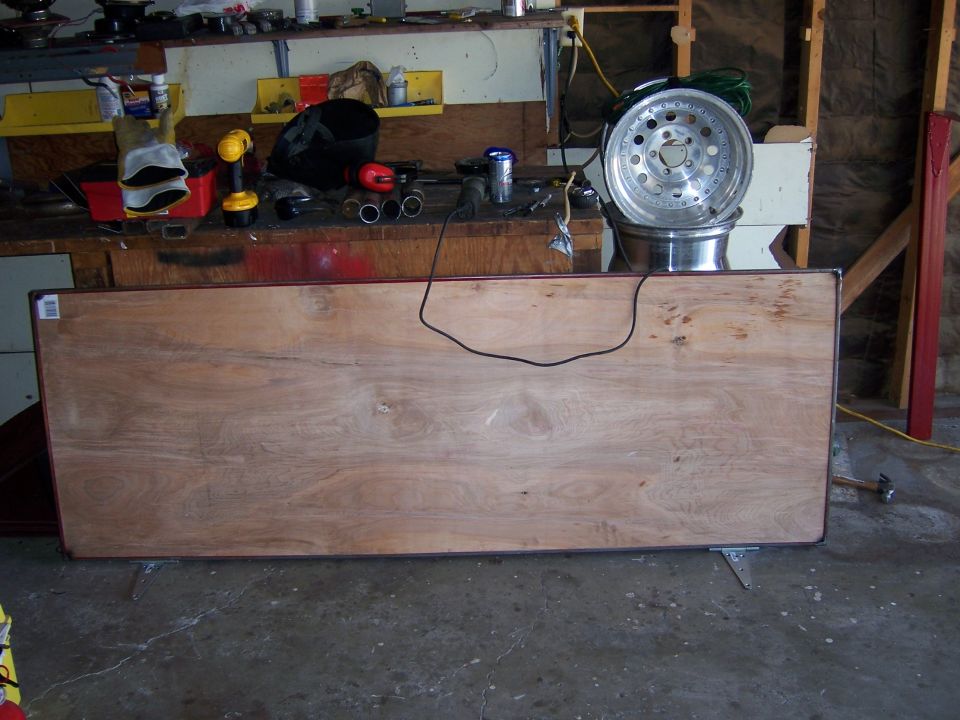 Workbench with drill, gloves, pipes, and a chrome car wheel stacked on another wheel