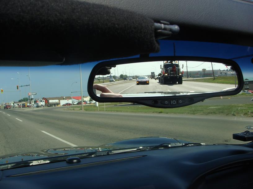 Red sports car in rearview mirror, following a semi-truck on highway