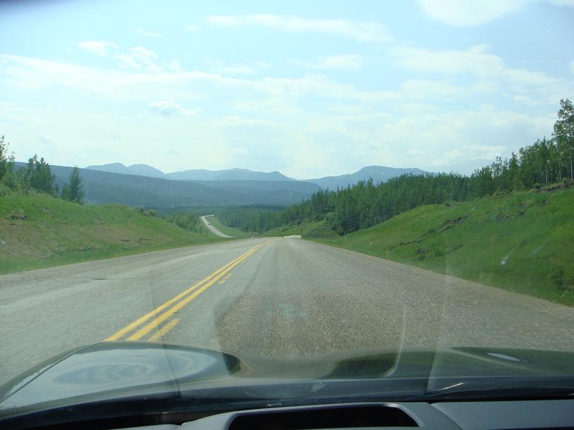 View from car dashboard looking out at a winding highway through a mountainous, forested landscape