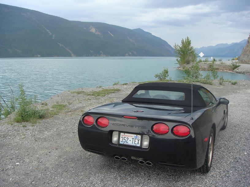 Black 2001 Chevrolet Corvette convertible parked on a gravel road by a lake, rear view