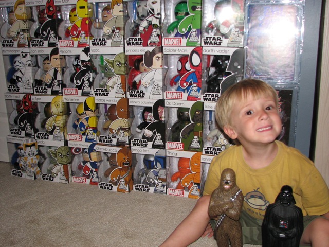 Child with Darth Vader and Chewbacca figures in front of Star Wars and Marvel toy collection