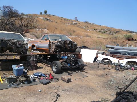 1975 Ford Ranchero - Two vehicles, including a 1975 Ford Ranchero, are disassembled in a junkyard setting with parts and tools visible.