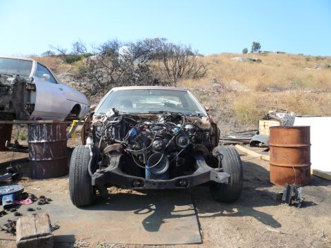 1975 Ford Ranchero - A dismantled vehicle sits in a junkyard setting, with another car partially visible behind it.