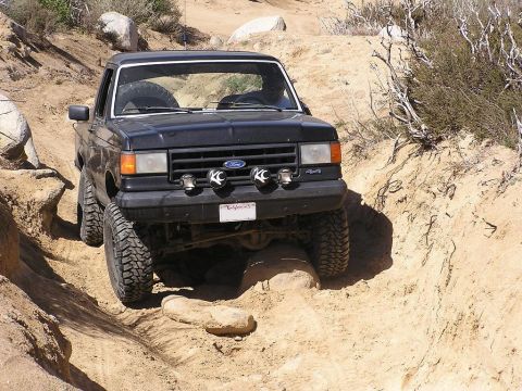 1990 Ford Bronco - A black Ford Bronco is shown off-roading on a challenging dirt path.