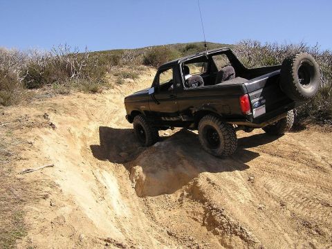 1990 Ford Bronco - This black Ford Bronco is navigating a steep, sandy trail with a clear blue sky overhead.