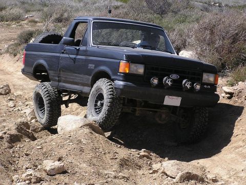 1990 Ford Bronco - This modified Ford Bronco is shown off-roading on a dirt path with large rocks.