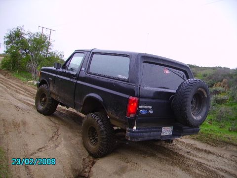 1990 Ford Bronco - A black Ford Bronco navigates a muddy trail, its rear tire mounted externally for off-road adventures.