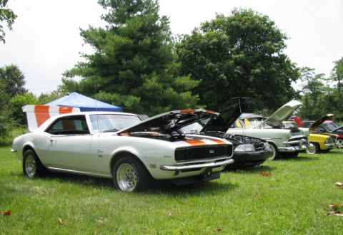 2003 Mercury Marauder - A white 1967 Chevrolet Camaro SS with orange stripes is displayed at a car show with its hood open, alongside other vehicles.
