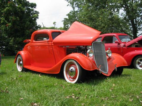 2003 Mercury Marauder - A classic orange hot rod coupe is parked on grass with its hood open, alongside another red car.