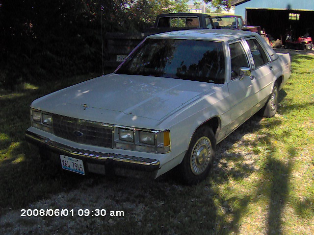 White 1980s Ford sedan, 3/4 front view. License plate X64 7945