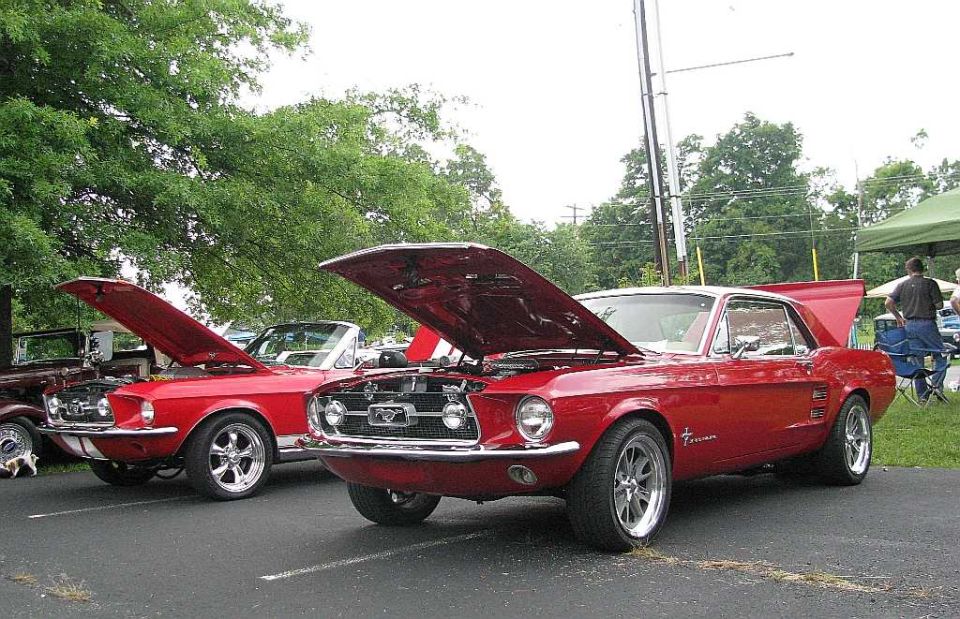 Two red Mustangs, one a coupe and one a convertible, parked with hoods open