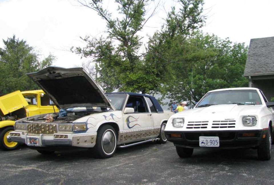 Two custom cars with hoods open, one white with flame decals and a skull, the other yellow.