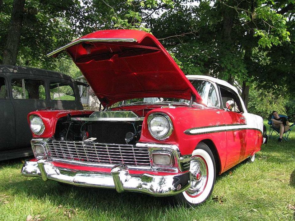 Red and white classic car with hood open, parked on grass.