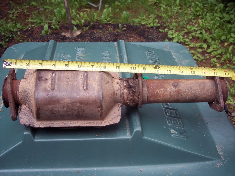 Rusty catalytic converter with measuring tape on a green surface