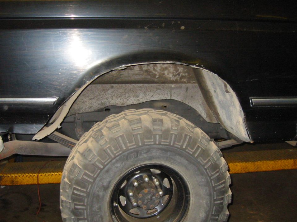 Cut rear wheel well on black Bronco with large Super Swamper tire on black wheel in a shop