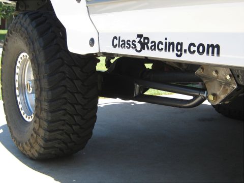 1996 Ford Bronco - Close-up of a white SUV's side, large off-road tires and the text "Class3Racing.com" alongside visible suspension components.