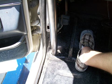 1990 Ford Bronco - Close-up view of the driver's side interior, focusing on the pedals and a roll cage.