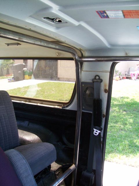 1990 Ford Bronco - The interior of a vehicle shows a roll cage and seat, with a view of the outdoors through the window.