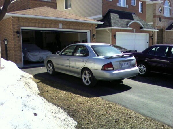 Silver sedan with a spoiler parked in a driveway, rear view. License plate is visible