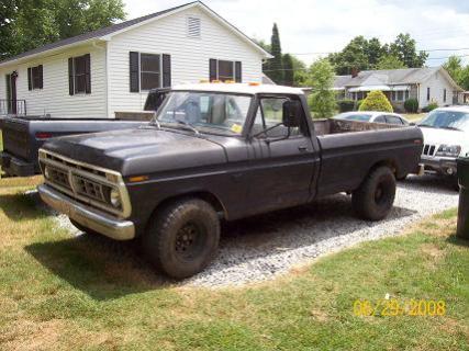 1979 Ford Bronco - A black pickup truck with a white roof is parked on gravel in front of a white house, with other vehicles nearby.