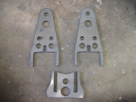 1992 Ford Mustang - Three metal brackets, likely for automotive repair or modification, are laid out on a concrete surface.