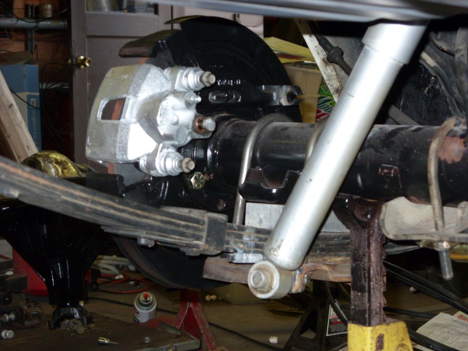 Rear axle assembly with silver brake caliper, black brake rotor, and leaf spring, supported by jack stands