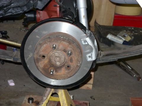 1978 Ford Mustang II - Close-up view of a vehicle's rear brake rotor and caliper, supported by a yellow jack stand in a garage setting.