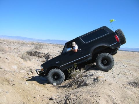 1992 Ford Bronco - A black Ford Bronco navigates a challenging off-road terrain under a clear blue sky.