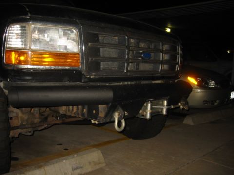 1995 Ford Bronco - Close-up of a black Ford truck's front end, showing the grille and headlights, with another vehicle visible behind.