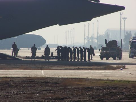 1995 Ford Bronco - Military personnel gather on an airfield next to a large transport aircraft and a tactical vehicle.