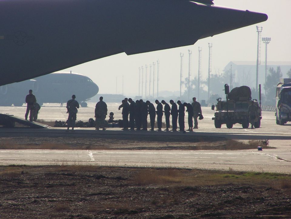Military personnel stand on an airfield near a large aircraft and a military vehicle
