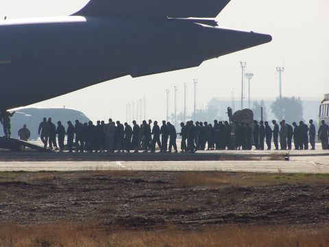 1995 Ford Bronco - A large aircraft dominates the foreground, casting a shadow over a group of people gathered on an airfield.