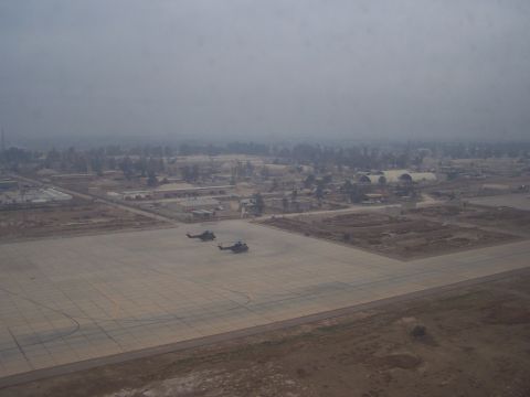1995 Ford Bronco - Two helicopters are parked on an airfield, with a town or base visible in the distance under a hazy sky.